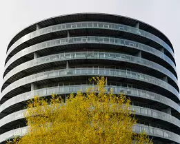 Balcony Rings Round glass-balconied tower of Gemini Residence rises behind a budding tree on a spring day in Copenhagen.