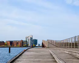 Curved Footbridge Wooden boardwalk sweeps over the harbor toward modern apartments in Copenhagen.