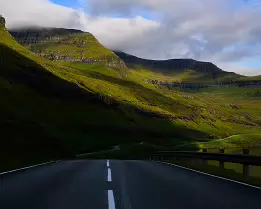 Endless Journey Winding road leading through green mountains under drifting clouds in the Faroe Islands.