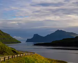 Seaside Path Curving road along a fjord with distant mountain silhouettes in the Faroe Islands.