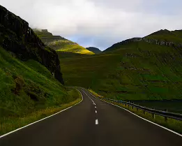 Hidden Route Empty road stretching through steep green valleys in the Faroe Islands.