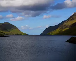 Calm Divide Narrow fjord flanked by sunlit and shadowed mountains in the Faroe Islands.