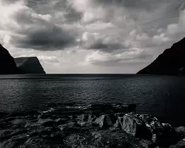 Stark Horizon Moody black and white view of a fjord with towering cliffs in the Faroe Islands.