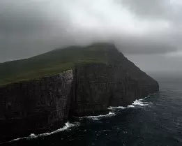 Dark Rise Misty cliff peak at Trælanípa rising steeply from the Atlantic in the Faroe Islands.