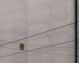 Warning Geometry Circular traffic sign indicating no left turn suspended on overhead wires against a plain building wall in Helsinki.