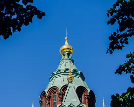 Orthodox Spires Uspenski Cathedral, a red brick Orthodox church with green roofs and golden domes, framed by leafy branches in Helsinki.