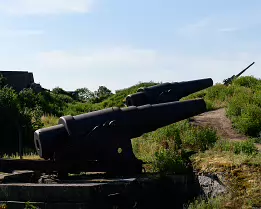 Coastal Sentinels Large black cannons on stone mounts surrounded by summer greenery on Länsi-Mustasaari Island in the Suomenlinna district of Helsinki.