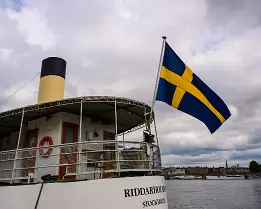 Swedish Waves A Swedish flag billows from a boat marked “Riddarholmen Stockholm” moored along the city waterfront.