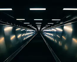 Tunnelbana Rise A long, lit escalator tunnel in Stockholm’s metro converges to a vanishing point deep underground.