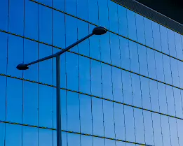 Urban Stillness Slim streetlamp silhouette set before a seamless blue glass curtain wall of a contemporary Vienna office block.
