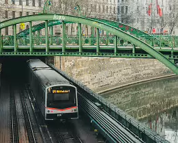Historic Span Vienna U4 metro train emerging from a tunnel beneath an ornate green iron bridge along the Wien River.