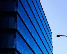Blue Minimalism Sharp corner of a blue glass office tower with a lone streetlamp silhouette against a pale Vienna sky.